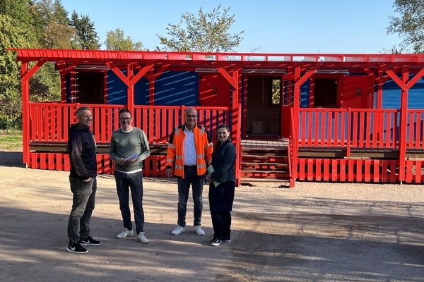 Rotblaue Kindergartenh&uuml;tte, davor vier Personen